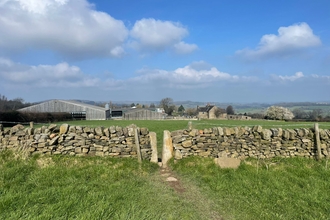 the view of farm buildings in the background with a dry stone wall in the foreground and a blue sky with a couple of clouds