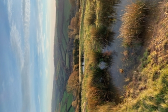 Hills and fields in the background with ponds in the foreground and a blue sky with a few clouds