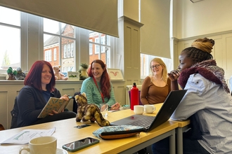 four women sat round a table working and laughing with each other